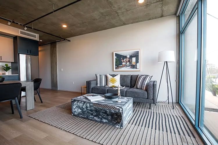 Living and dining room of a finished one-bedroom loft, with a board-formed concrete ceiling and a full-height window wall.